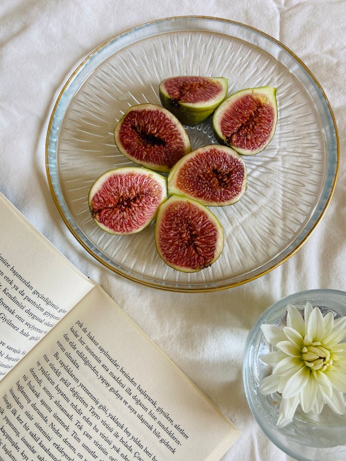 Overhead view of sliced figs on a plate, with an open book and flower, creating a cozy setting.